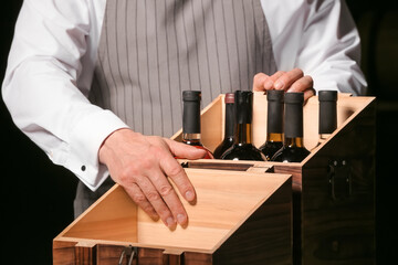 Man with bottles of wine in box on dark background