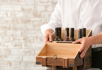 Man with bottles of wine in box on brick background