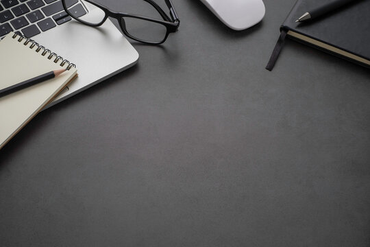 Workplace office with dark grey desk. Close-up view from above of keyboard, glasses with notebook and mouse. Tabletop space for creative work. Flat lay with copy space. Business and finance concept.