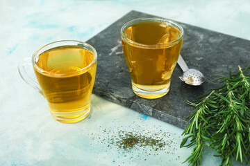 Cups of hot tea with rosemary on color background