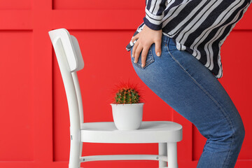 Young woman and chair with cactus on color background. Hemorrhoids concept