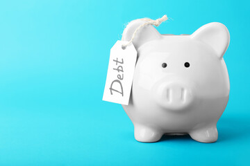 Piggy bank and tag with word DEBT on color background