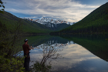 Fototapeta na wymiar Fisherman at Lake Stanton with reflections of Great Northern Mountain in background