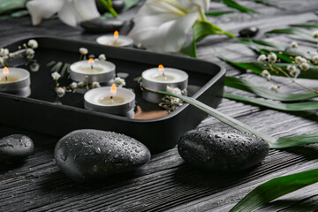 Spa stones and plate with water and candles on dark wooden background. Zen concept