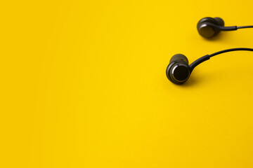Black earphone on yellow background with copy space. Music and lifestyle concept.