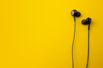 Black earphones on yellow background. In-ear headphones style for portable devices.