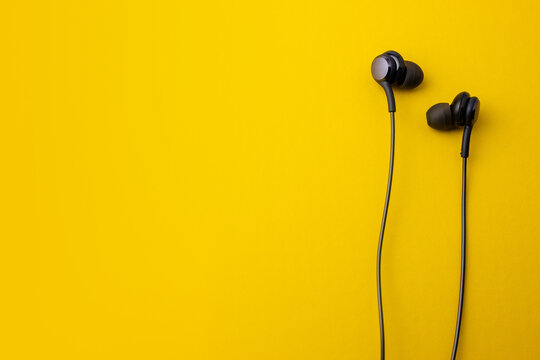 Black earphones on yellow background. In-ear headphones style for portable devices.