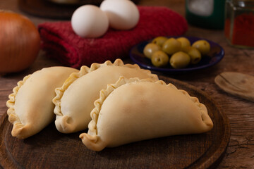 La tradicional empanada de carne argentina, sus ingredientes, carne, huevo, cebolla, aceituna y condimentos tabla de madera rústica