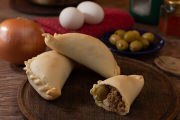 La tradicional empanada de carne argentina, sus ingredientes, carne, huevo, cebolla, aceituna y condimentos tabla de madera rústica