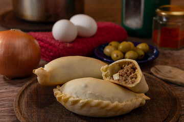 La tradicional empanada de carne argentina, sus ingredientes, carne, huevo, cebolla, aceituna y condimentos tabla de madera rústica