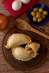 La tradicional empanada de carne argentina, sus ingredientes, carne, huevo, cebolla, aceituna y condimentos tabla de madera rústica