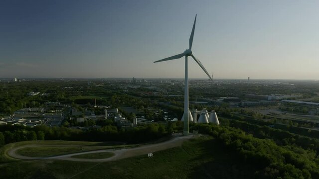 Aerial view, flying around a windmill producing green energy near the Allianz Arena in Munich, Germany.