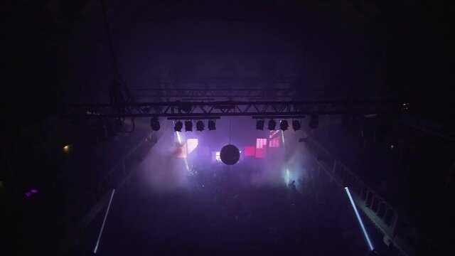 Overlooking people inside a night club, purple lights blinking at techno rave in big crowded concert- Pan view