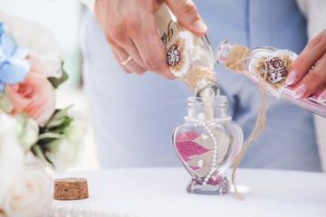 Bride and groom pouring colorful different colored sands into the crystal vase close up during symbolic nautical decor destination wedding marriage ceremony on sandy beach in front of the ocean 