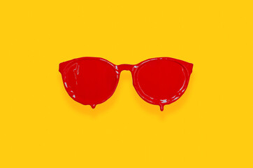 Red poster color painted on sunglasses with yellow background. Minimal summer concept.