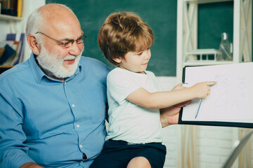 Portrait of grandfather and grandson on blackboard in classroom. Kid with old teacher learning in class on background of blackboard. Father and son.
