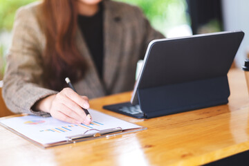 Closeup image of a beautiful asian businesswoman working and using digital tablet as a computer pc with financial document on the table