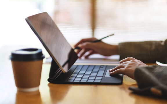 Closeup image of a businesswoman working and typing on tablet keyboard as a computer pc with coffee cup on the table