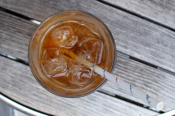Glass of iced tea top view on a wooden table. Iced iced tea has a paper straw to protect nature. Paper straw can be recycled.