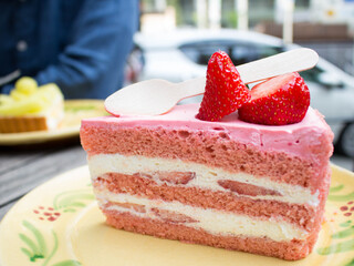 Strawberry cake on a yellow plate with a wooden spoon. A piece of pink strawberry cake on a table in a cafe on the street. The spoon in the cafe is made from recyclable wood material.