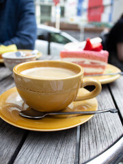 Cup of coffee with a strawberry cake on wooden table in cafe outside