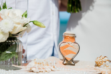 Bride and groom pouring colorful different colored sands into the crystal vase close up during symbolic nautical decor destination wedding marriage ceremony on sandy beach in front of the ocean 