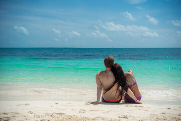 A man and a woman are sitting on the seashore and looking at the horizon.