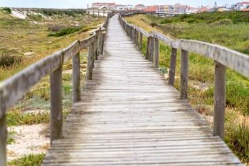 Fototapeta na wymiar Wooden path at over sand dunes. Wooden footbridge of Costa Nova beach in Aveiro, Portugal.