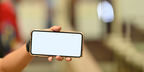 Cropped image of woman holding a white blank screen smartphone in horizontal. Hands holding mobile with empty screen for advertisement concept.