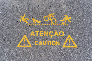 Inscription on asphalt road with yellow warning signs and text on portulal language " Attention Caution'