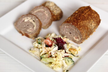 Meat roulade with salad on plate. Rolled meat with a filling of cheese and ham.