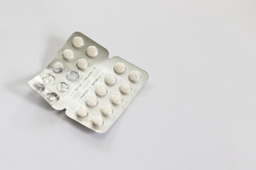 Foil packet of antihistamines with used pills. Small white pills on a white background