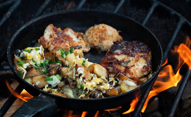 Potatoes with mushrooms and eggs and a chop of turkey fillet are fried in a pan over a fire