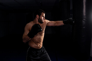 Fototapeta na wymiar boxer on a dark background beats a direct hit in a boxing bag photo for a fitness club