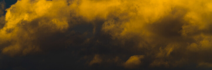 Panorama beautiful golden fluffy clouds illuminated by disappearing rays at sunset, thunderclouds floating across sunny blue sky to change season weather. Soft focus, motion blur sky landscape.