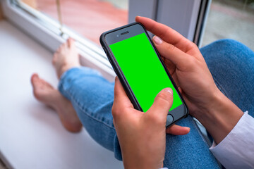 girl holding a phone with a green background for replacement. Online shopping. Loves social networks. remote work. Browses websites on your phone.