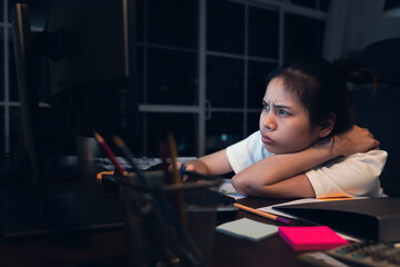 Stressful Asian business woman sitting on the chair and look at the computer screen on office at night.