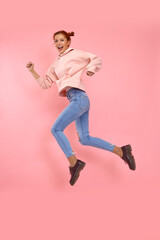 Fototapeta na wymiar Full length body shot of incendiary cheerful emotional beautiful young woman in casual clothes jump high in a running pose on a pink background in the studio. Concept of pursuit of career and success