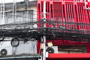 Electrical wiring post in thailand. A huge number of wires on a pole. Against the background of a red and white building