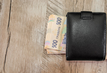 500 hryvnia in a black men's wallet on a wooden background. View from above. Copy space. Place for text.