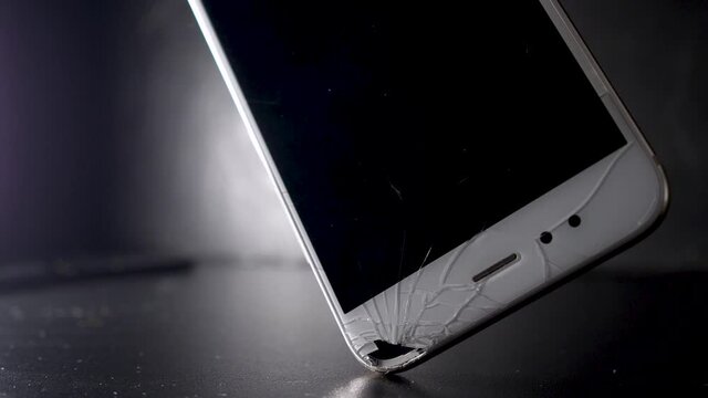 broken smartphone screen, a hand picks up a phone with a cracked display. black background