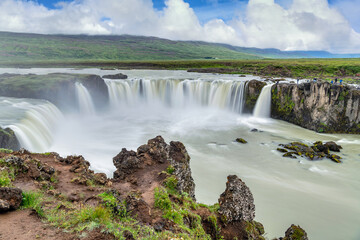 Godafoss Falls in the summer, green grass colors and tourists This is a famous and popular tourist destination in Iceland.