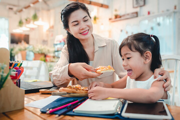 Asian mothers and children do activities at home. Mother is going to feed pizza for her kids who are doing homework and studying online at home. During the virus epidemic, Covid-19