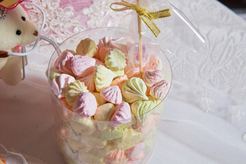 candy in a plastic glass pink and yellow color . colorful marshmallow candies in plastic container on a white background.