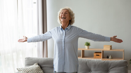 Lively hoary 65s aged woman stands in modern living room stretched hands feeling happiness and...