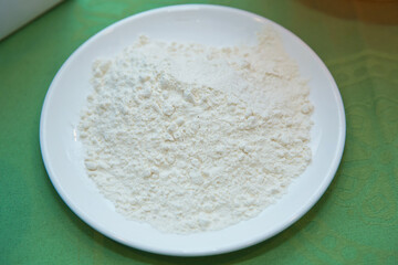 Wheat flour in a plate on green background . The flour is green background on the white plate .