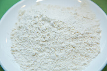 Wheat flour in a plate on green background . The flour is green background on the white plate .