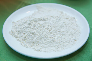 Wheat flour in a plate on green background . The flour is green background on the white plate .