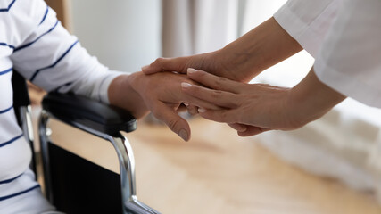 Disabled elderly woman sitting in invalid carriage her palm holding stroking caring nurse close up image. Physical disorder caused by senile diseases, Alzheimer or Parkinson, homecare medicare concept