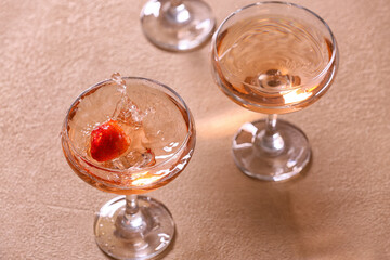 Strawberry falling into glass of tasty champagne on table